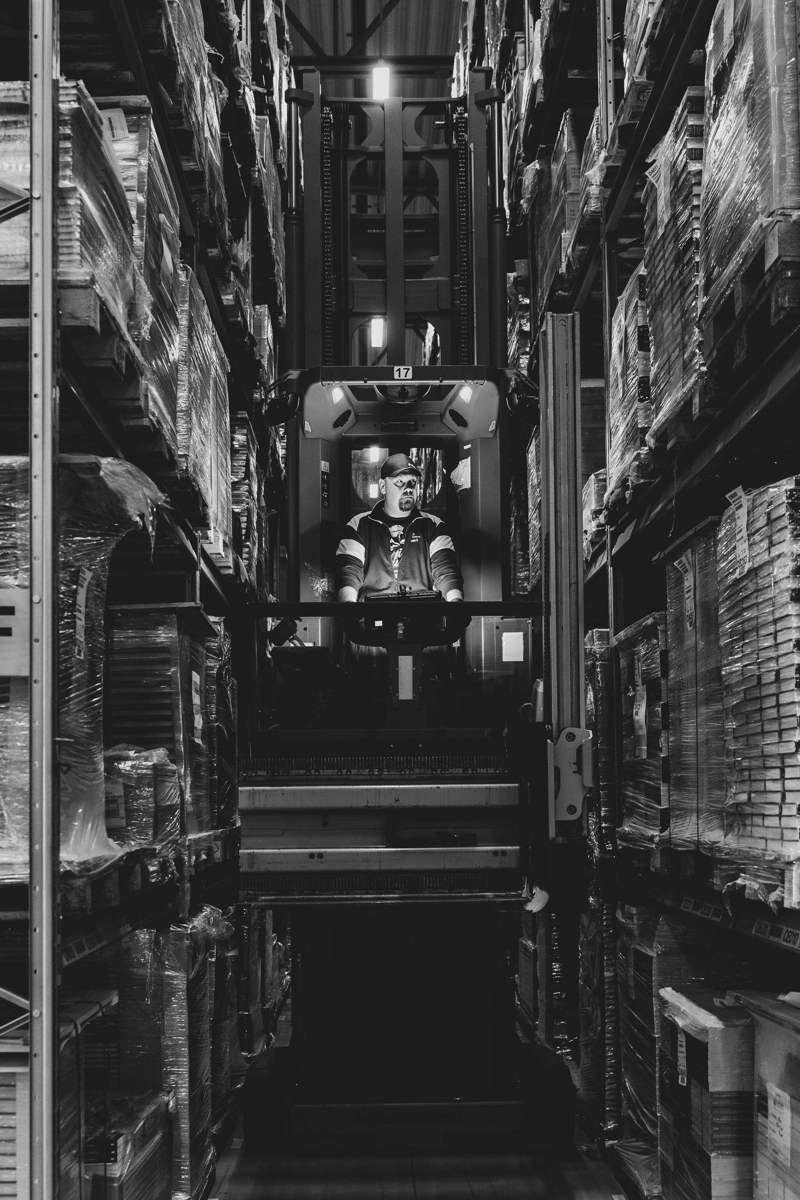 Black-and-white photograph of a lift-truck operator working between racks of wrapped goods